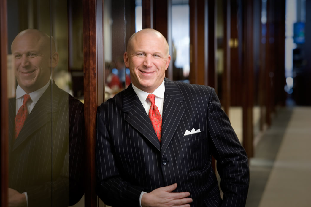 Portrait of a man in a pin stripe suit leaning against a glass wall.