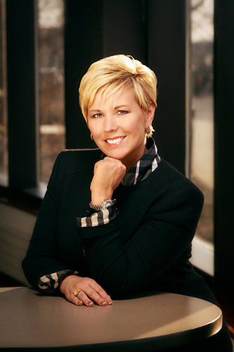 A female executive in a dark suit, resting her chin on her hand.